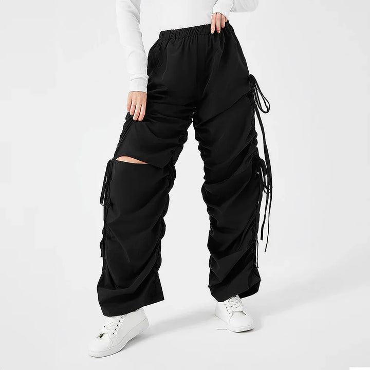 Woman wearing black ruched wide-leg pants with white sneakers on white background