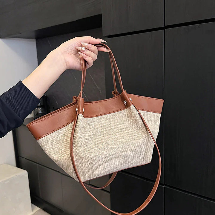 Hand holding beige canvas and brown leather tote bag with long handles against black cabinet