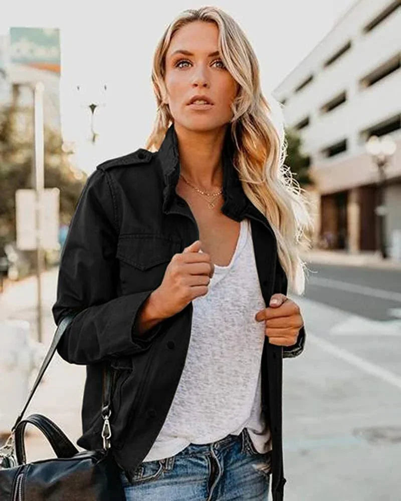 Blonde woman in black jacket, white shirt, and jeans holding black handbag on urban street