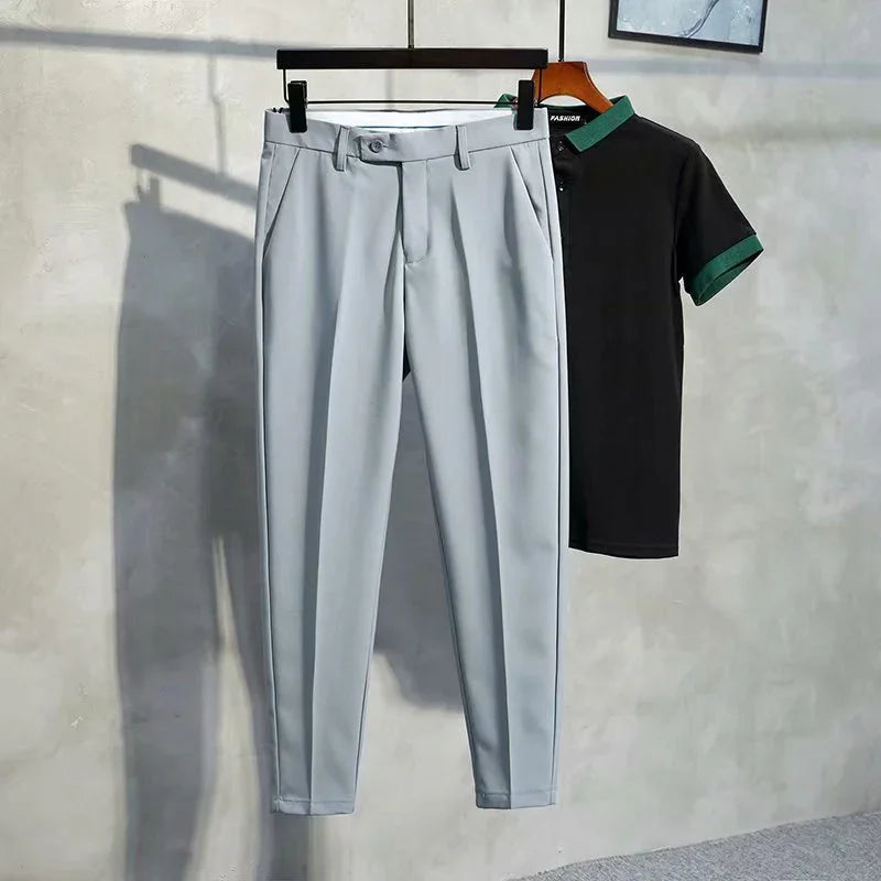 Light gray tailored pants and black polo shirt with green collar and sleeve cuffs hanging on wall