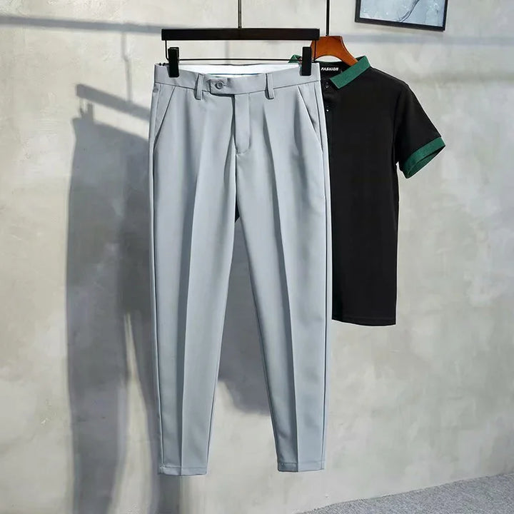 Light gray tailored pants and black polo shirt with green collar and sleeve cuffs hanging on wall