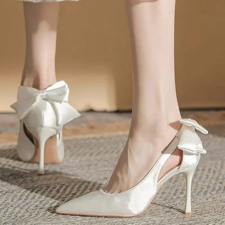 Elegant white satin high heels with pointed toes and large bow detail on the back
