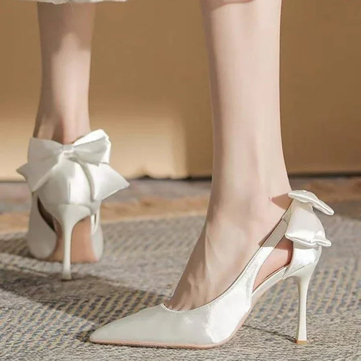 Elegant white satin high heels with pointed toes and large bow detail on the back