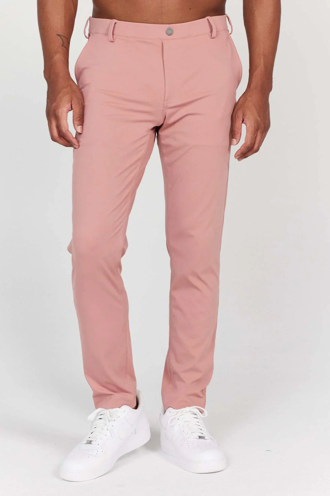 Men's slim fit pink chinos styled with white sneakers against white background