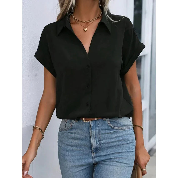 Woman wearing black short sleeve button-up blouse with blue jeans and gold jewelry