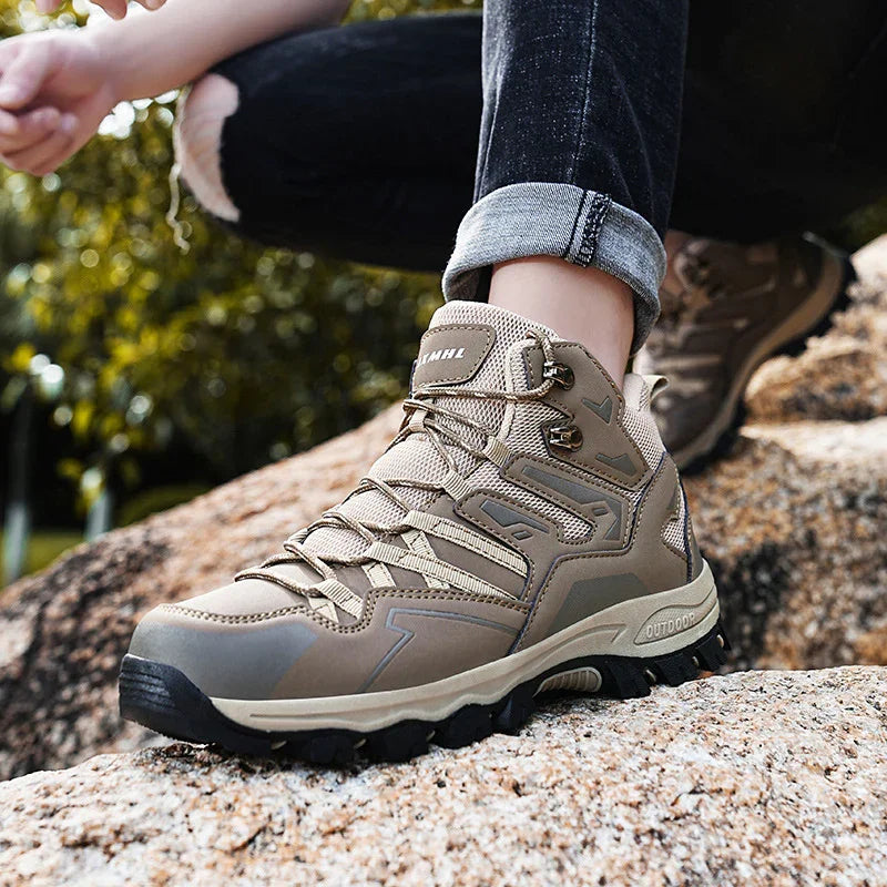 Close-up of beige outdoor hiking boots worn with rolled-up black jeans on rocky terrain