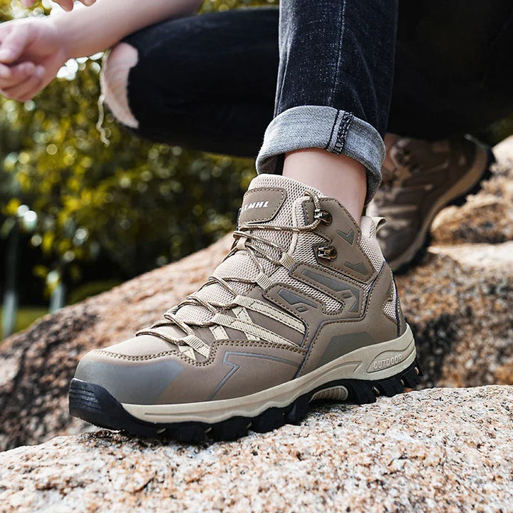 Close-up of beige outdoor hiking boots worn with rolled-up black jeans on rocky terrain