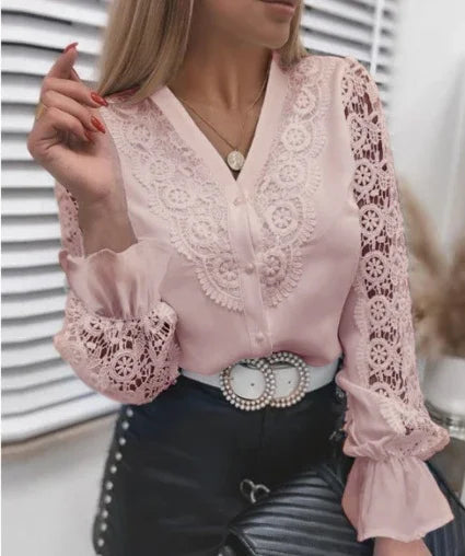 Woman wearing a pale pink lace blouse with intricate floral patterns and black pants with pearl buttons