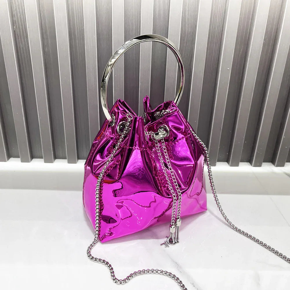 Shiny metallic pink bucket handbag with silver chain strap and circular metal handle on white marble