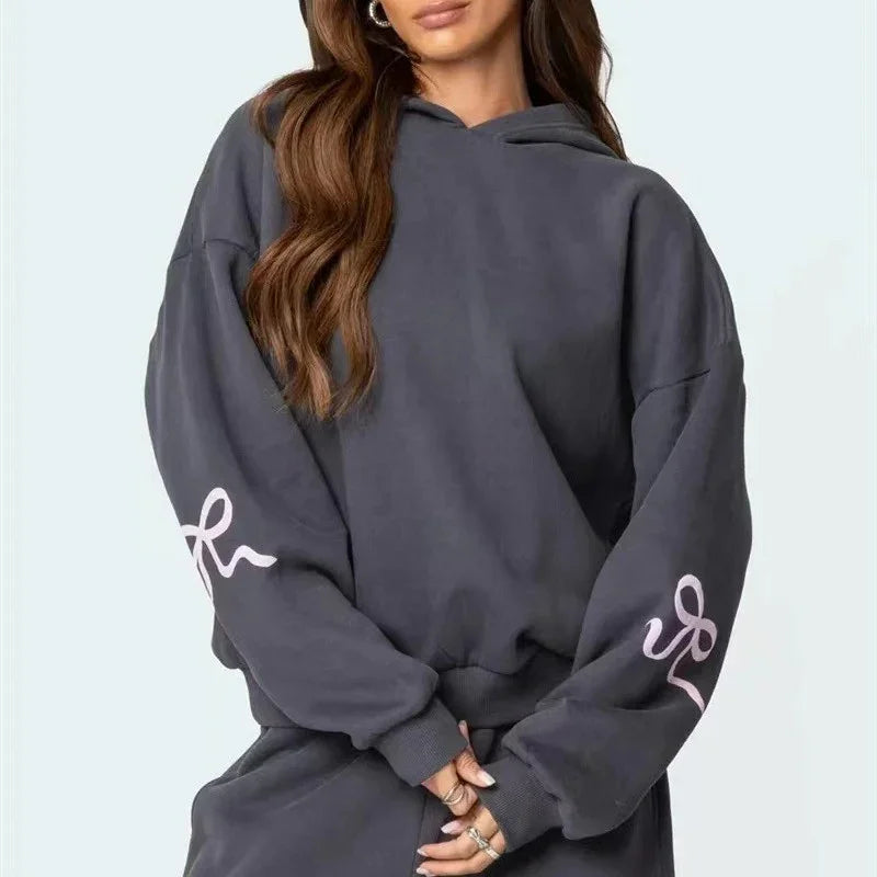 Woman wearing oversized dark gray hoodie with pink sleeve design and matching pants