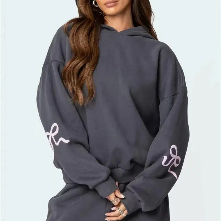 Woman wearing oversized dark gray hoodie with pink sleeve design and matching pants