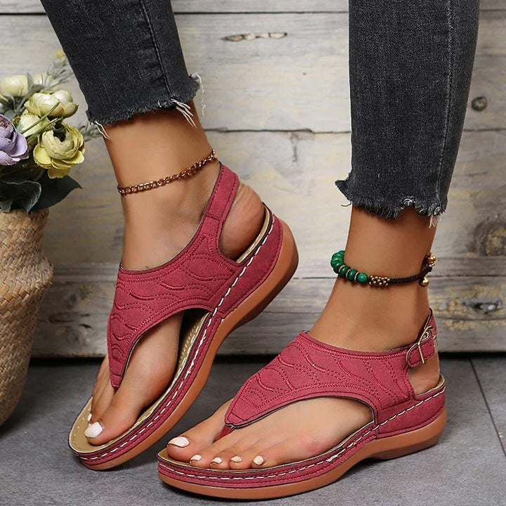 Women's stylish red open-toe sandals with ankle straps and stitching detail on feet wearing black frayed jeans