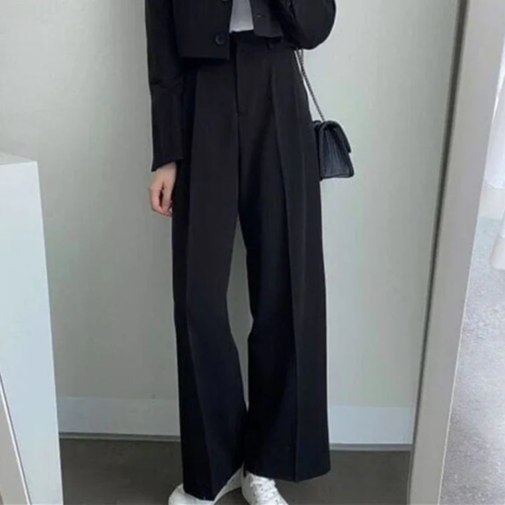 Woman wearing black wide-leg trousers and cropped jacket with white sneakers and black shoulder bag