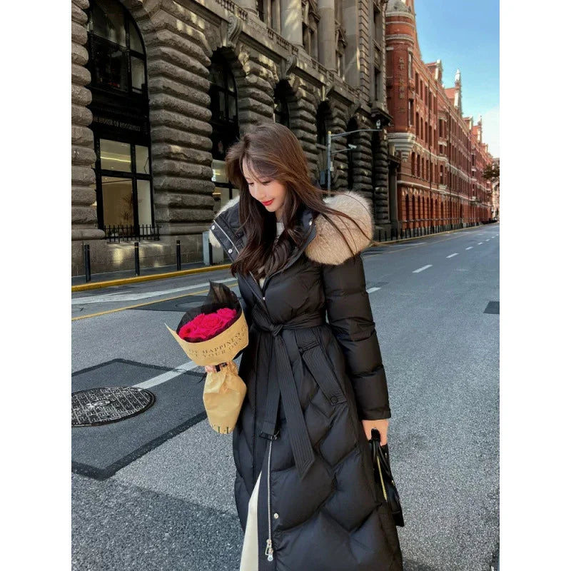 Woman in long black puffer coat with fur hood holding red rose bouquet on city street
