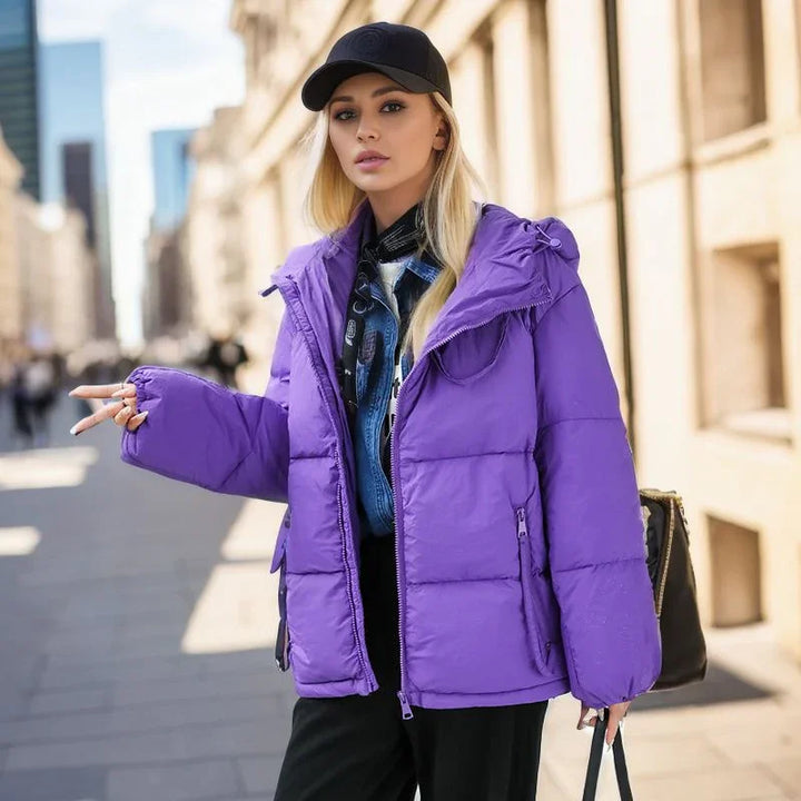 Young woman wearing a purple puffer jacket and black cap walking in urban street setting