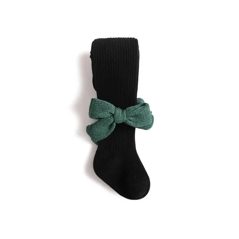 Black ribbed knee-high sock with green textured fabric bow accessory on white background