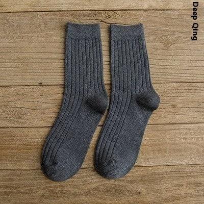 Pair of dark gray ribbed knit wool socks laid flat on wooden surface, cozy warm footwear