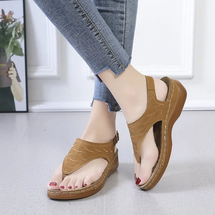 Casual brown leather wedge sandals worn with blue skinny jeans on a gray floor