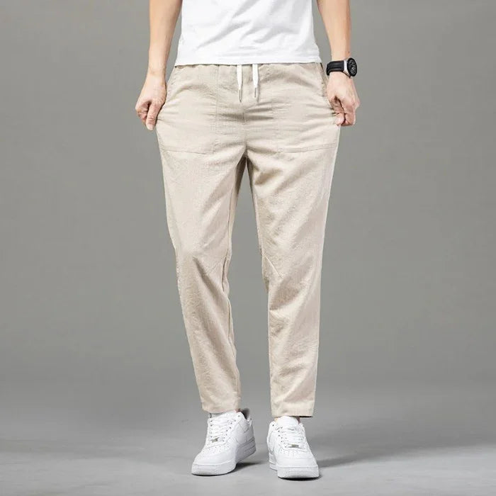 Person wearing beige casual drawstring pants and white sneakers on gray background