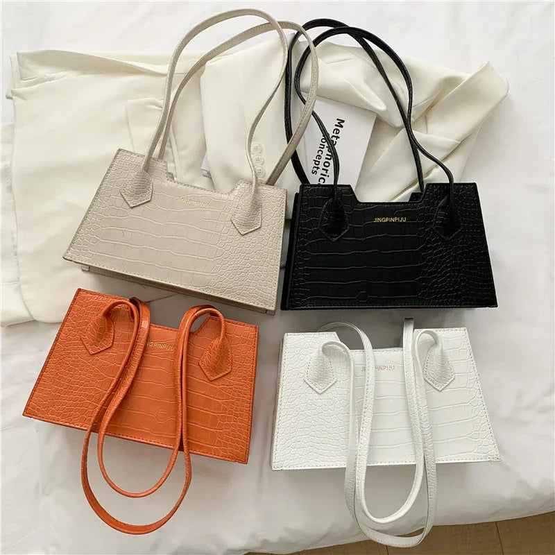 Four crocodile texture leather handbags in beige, black, orange, and white laid on white fabric
