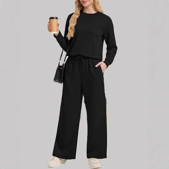 Woman wearing black casual loungewear set with long sleeves and wide-leg pants, holding coffee cup