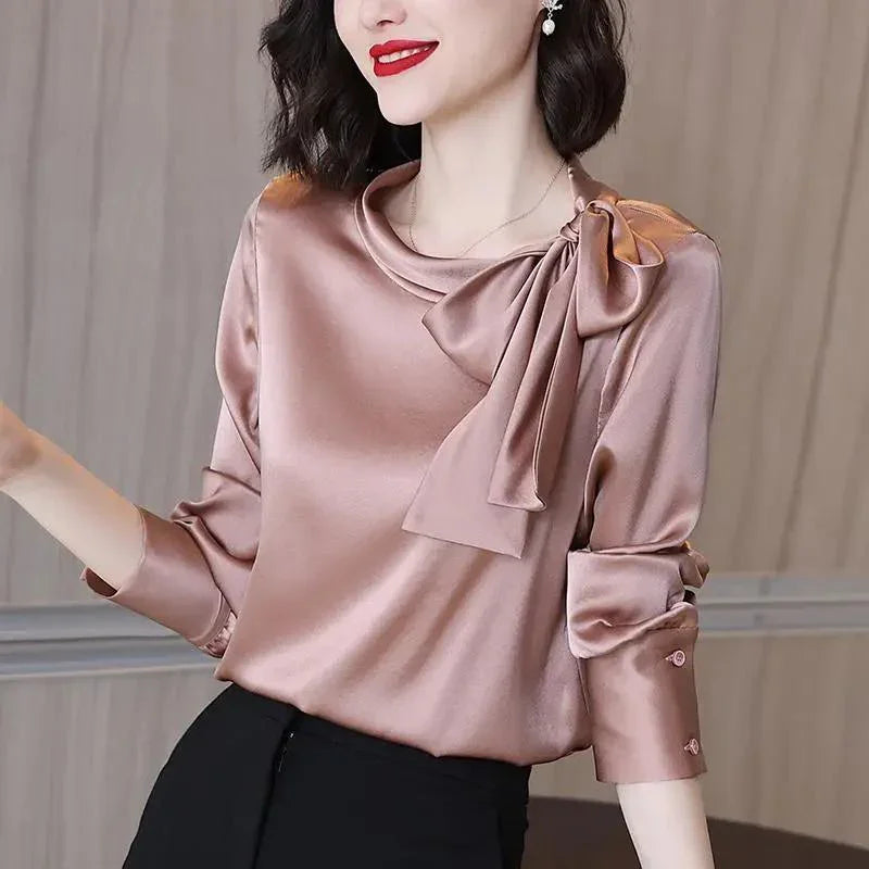 Woman wearing a shiny satin mauve blouse with a large bow on the shoulder and rolled-up sleeves