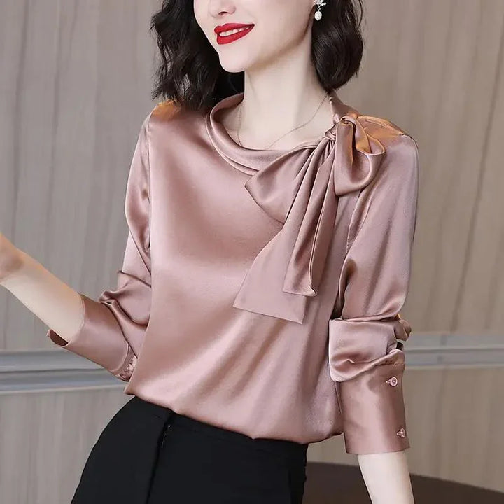 Woman wearing a shiny satin mauve blouse with a large bow on the shoulder and rolled-up sleeves