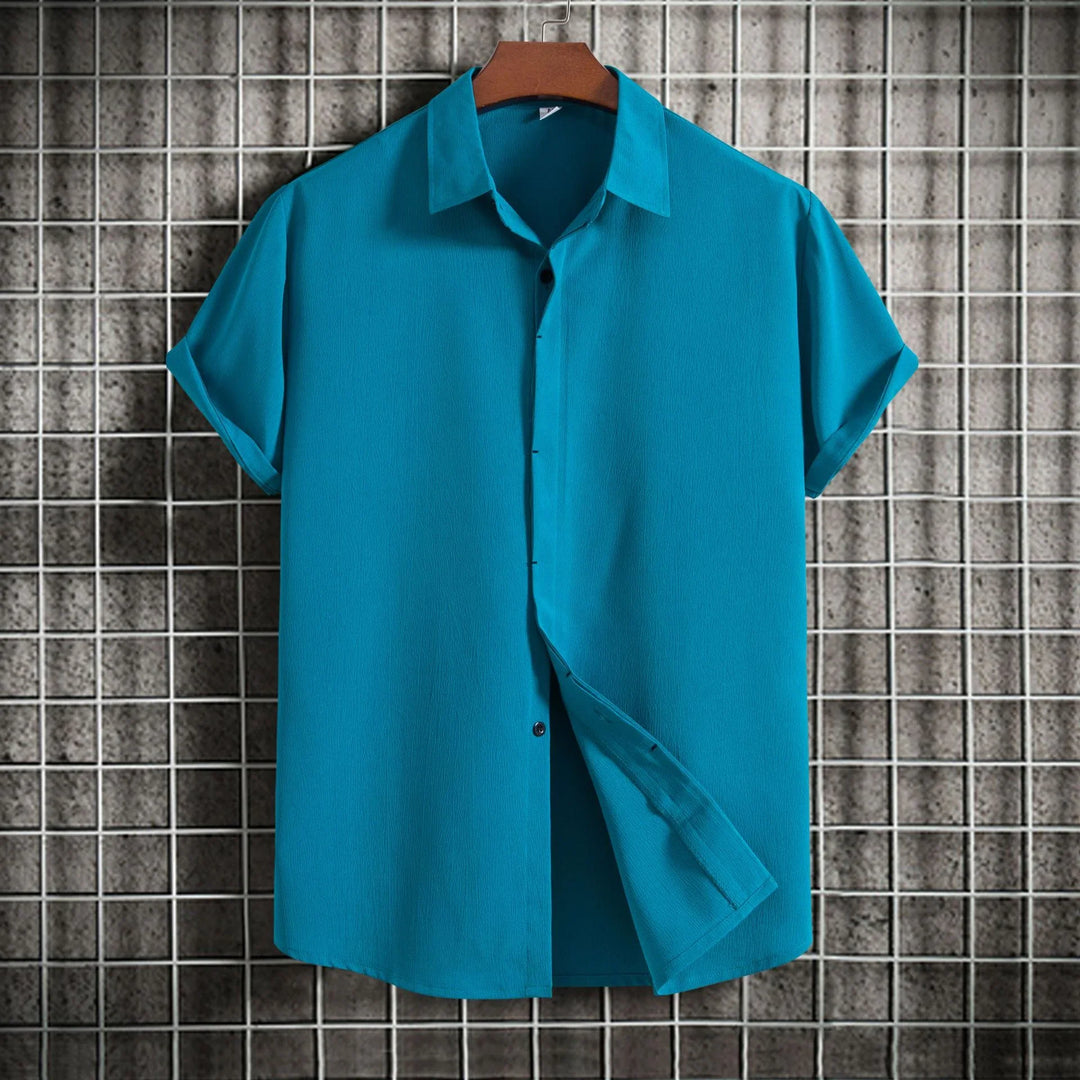 Teal short sleeve button-up shirt on hanger against metal grid and concrete background