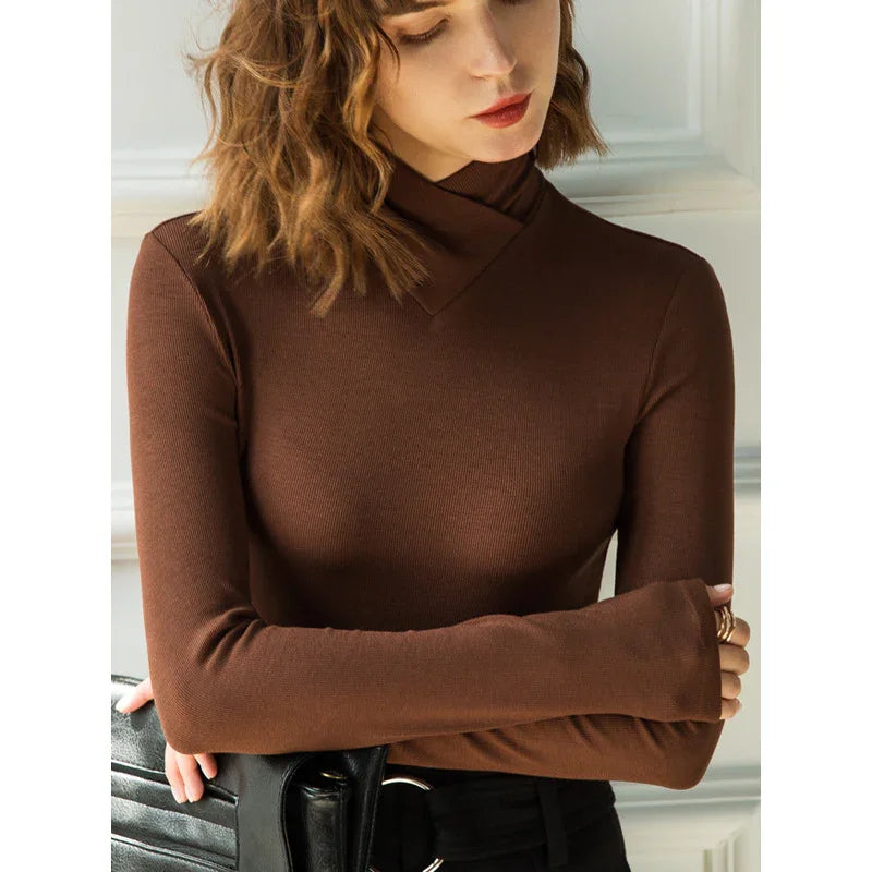 Woman wearing a brown long-sleeve ribbed sweater with a unique neckline, holding black leather bag