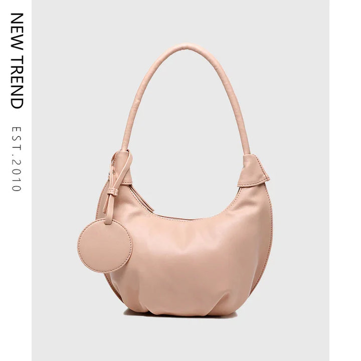 New trend blush pink leather shoulder bag with round tag against gray background