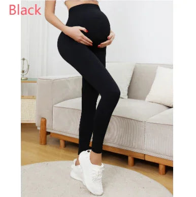 Pregnant woman wearing black maternity leggings and white sneakers in modern living room