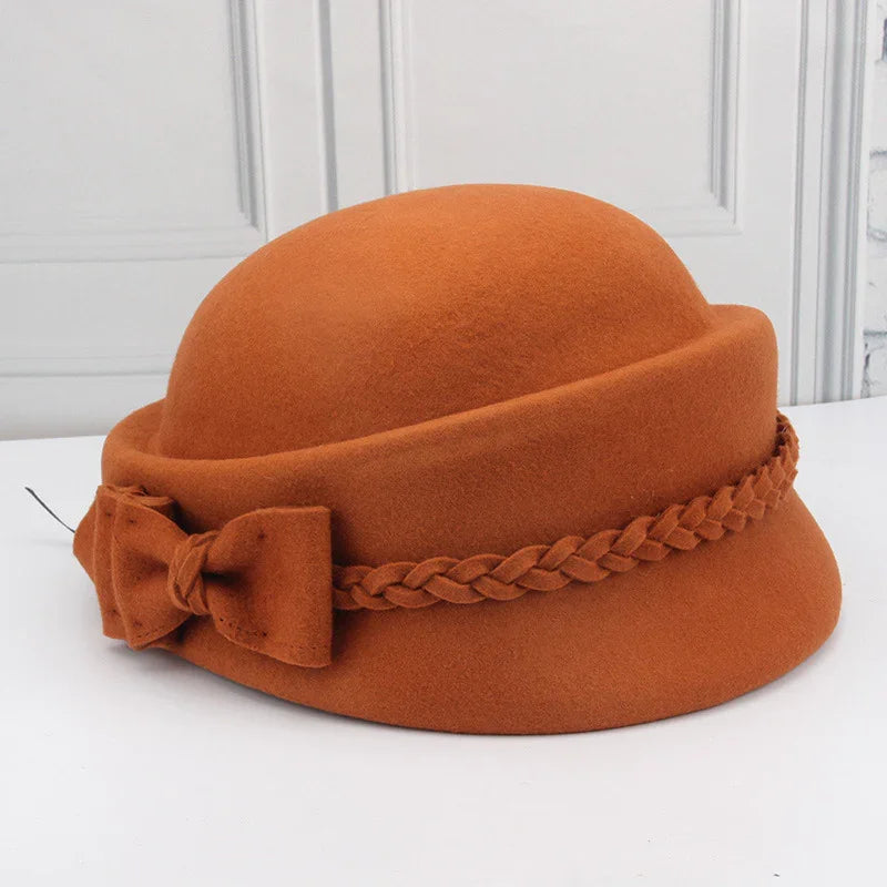 Rust orange felt cloche hat with braided band and decorative bow on white surface