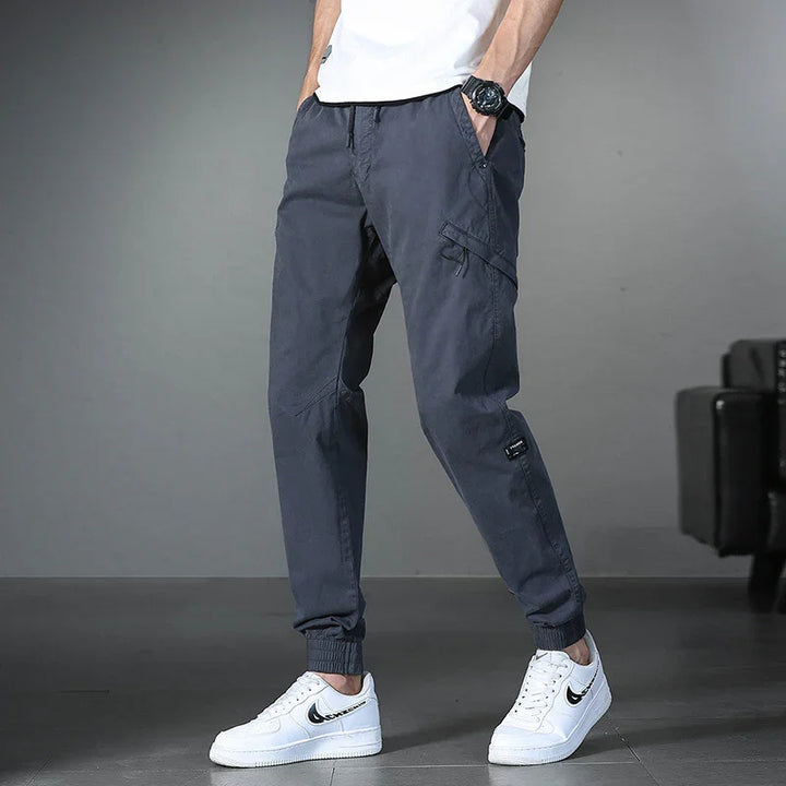 Men's casual dark gray cargo jogger pants with elastic cuffs and front pockets, paired with white sneakers