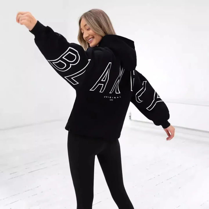 Smiling woman in black oversized hoodie and leggings posing in bright studio