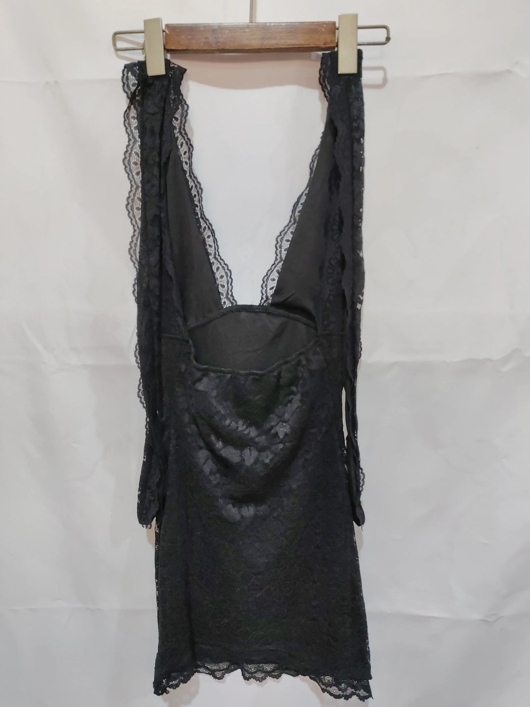Black lace slip dress with deep V-neck hanging on wooden hanger against white background