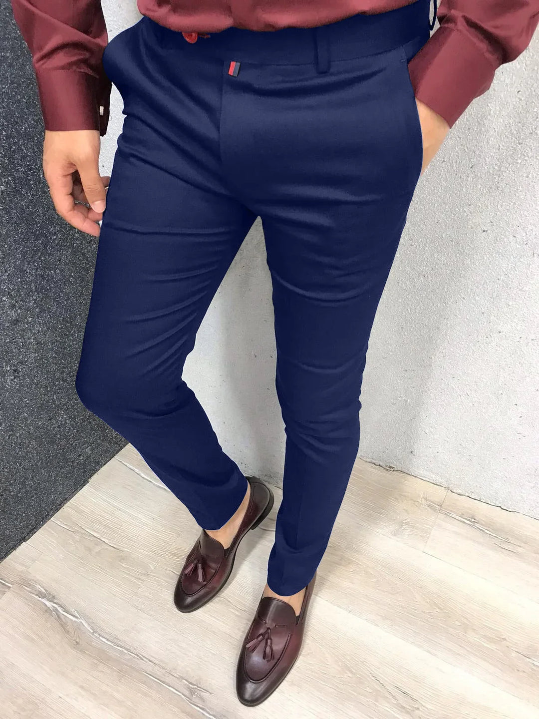Man wearing slim fit navy blue dress pants paired with brown tassel loafers on light wood floor