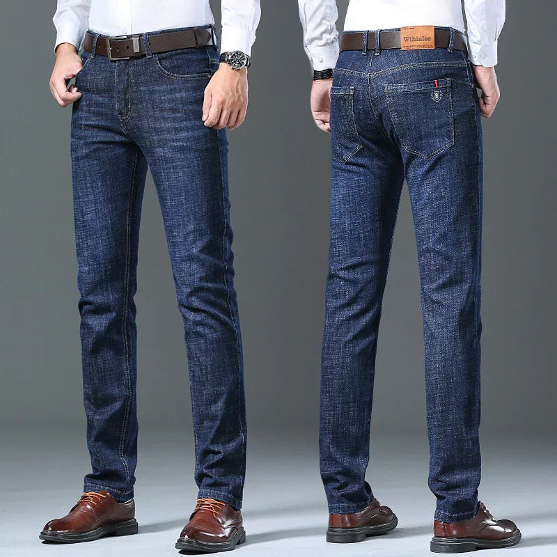Men's slim fit dark blue jeans styled with brown leather belt and brown dress shoes on gray background