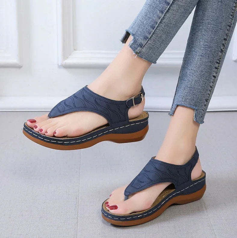 Woman wearing navy blue cushioned platform thong sandals paired with frayed hem jeans on gray floor