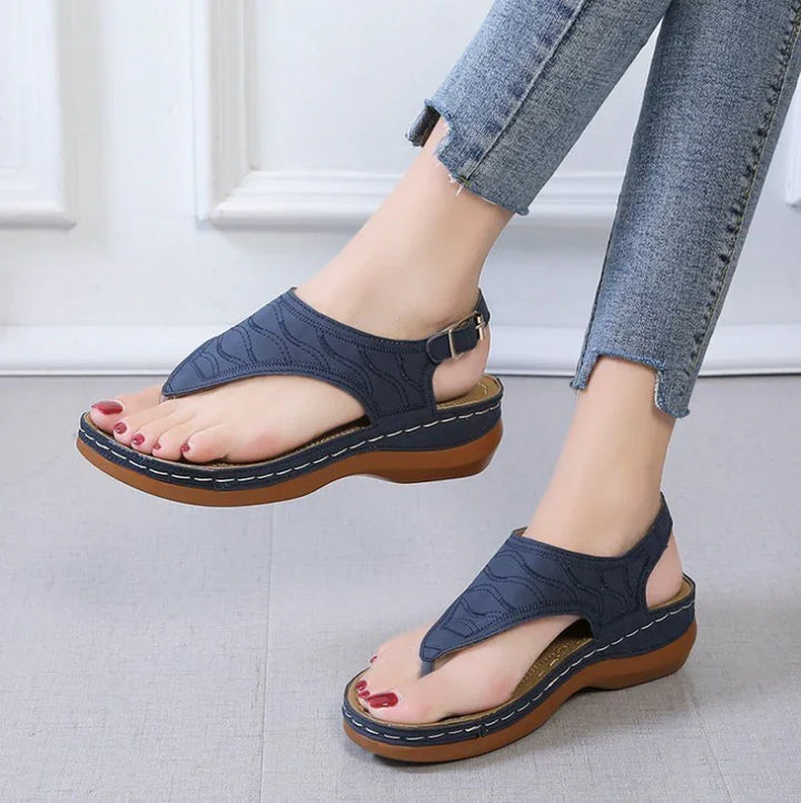 Woman wearing navy blue cushioned platform thong sandals paired with frayed hem jeans on gray floor