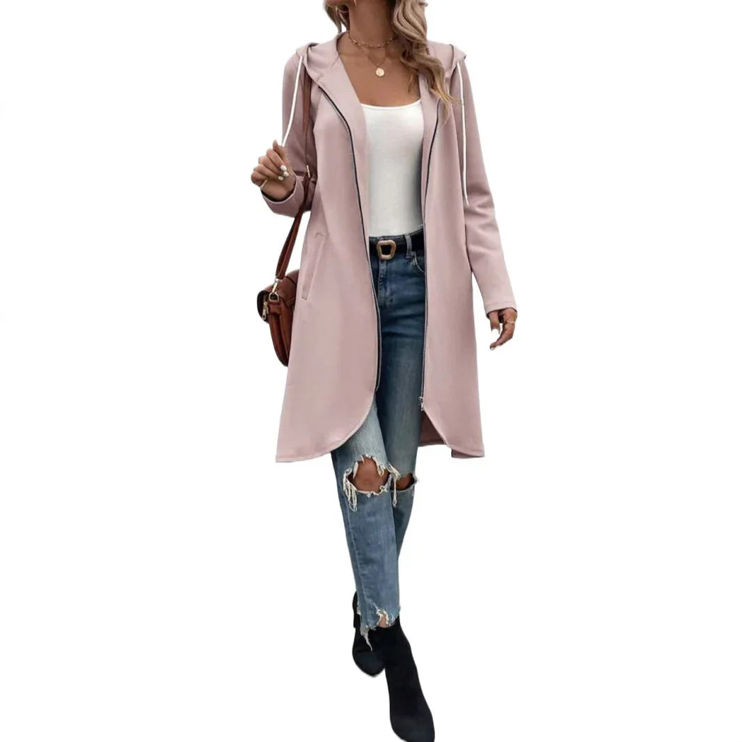 Woman wearing light pink hooded long coat, white top, ripped blue jeans, black boots, and brown shoulder bag