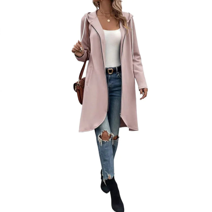 Woman wearing light pink hooded long coat, white top, ripped blue jeans, black boots, and brown shoulder bag