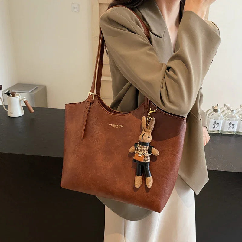 Woman in beige blazer holding brown leather tote bag with rabbit keychain in modern interior