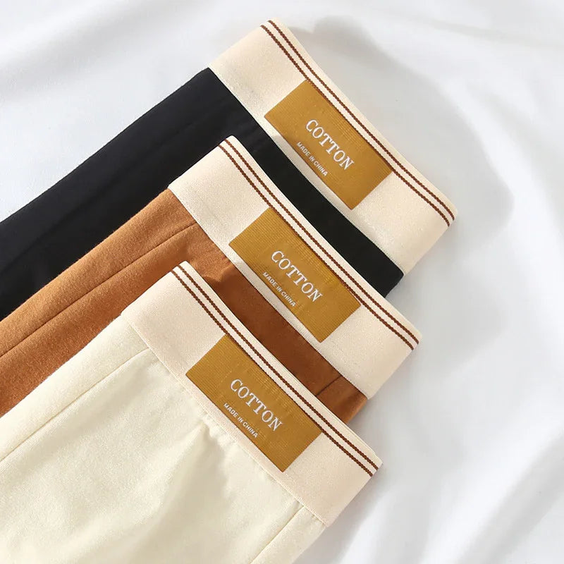 Stack of cotton fabric pants in black, brown, and cream with beige elastic waistbands labeled cotton