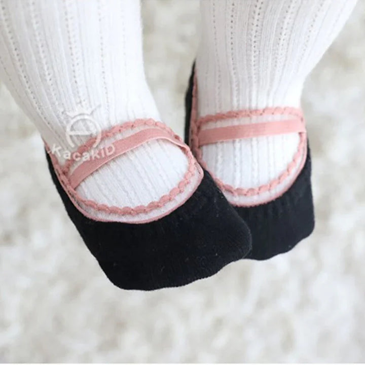 Close-up of baby feet wearing black and pink Mary Jane style socks with white ribbed tights