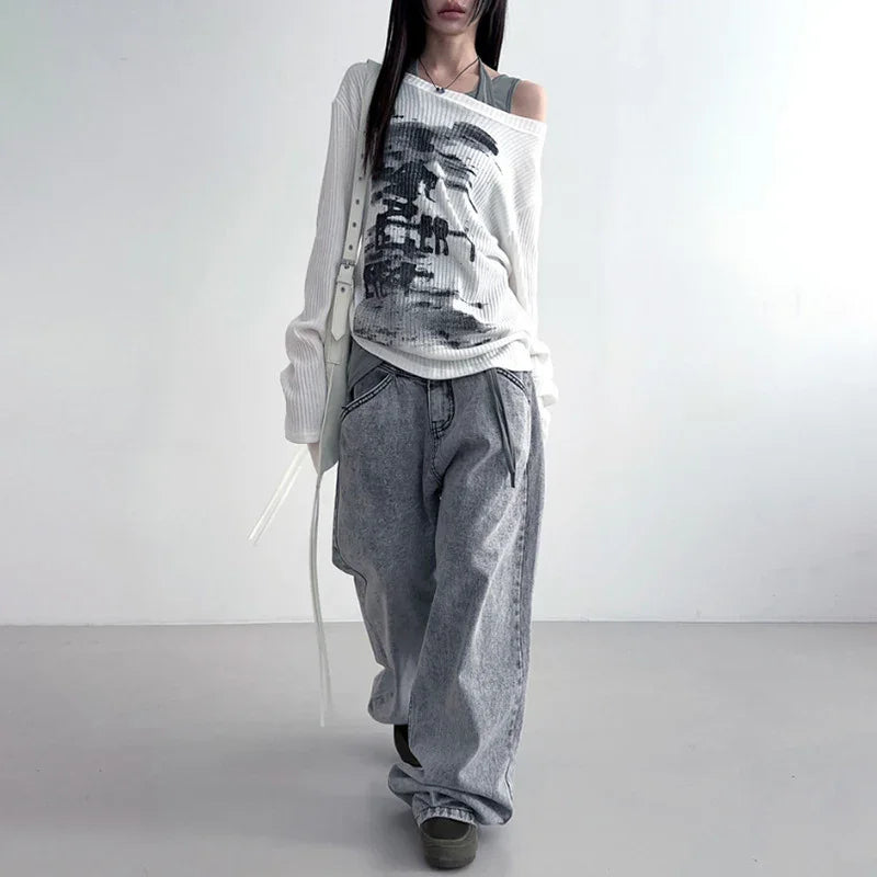 Woman wearing off-shoulder white sweater with graphic print and loose gray jeans in minimalist setting