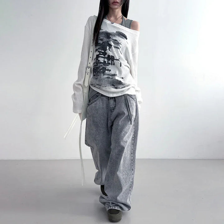 Woman wearing off-shoulder white sweater with graphic print and loose gray jeans in minimalist setting