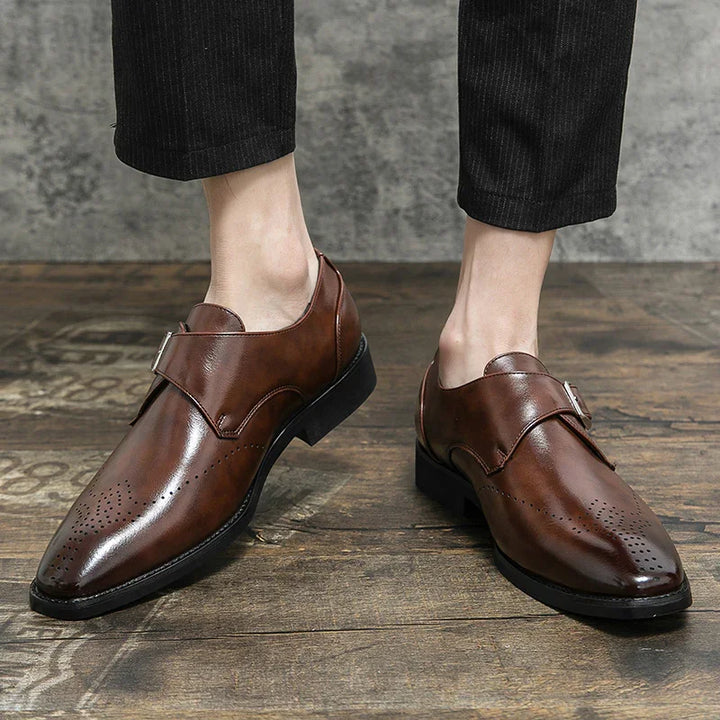 Men's brown leather monk strap dress shoes with perforated toe detail on wooden floor
