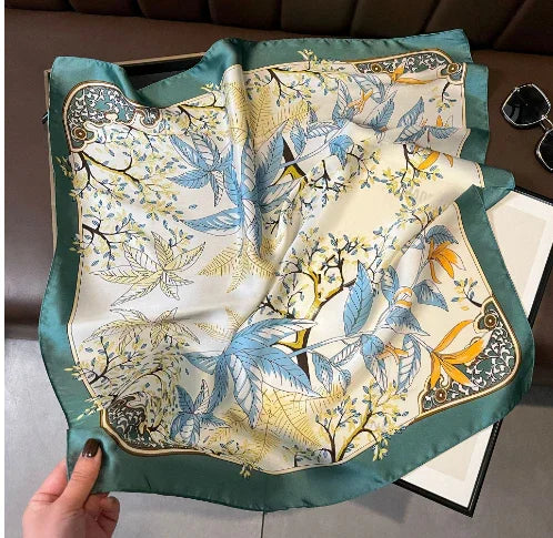 silk scarf with botanical print in shades of blue, yellow, and green on a soft green border