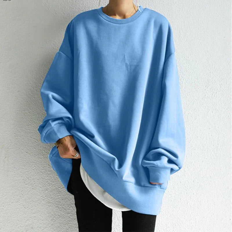 Person wearing oversized light blue sweatshirt with long sleeves and white shirt underneath against white wall