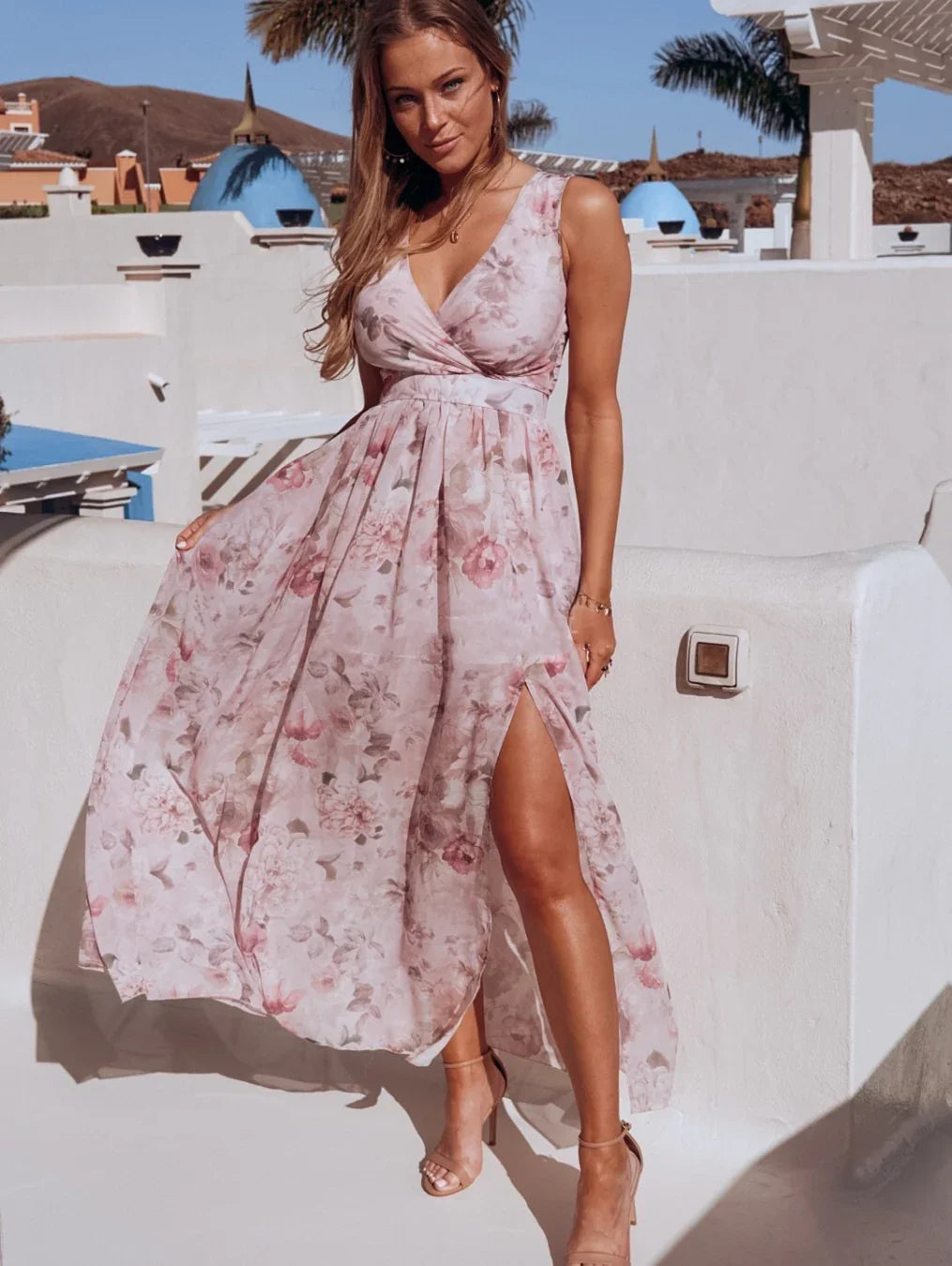 Woman wearing sleeveless floral midi dress with side slit posing outdoors in sunny Mediterranean setting